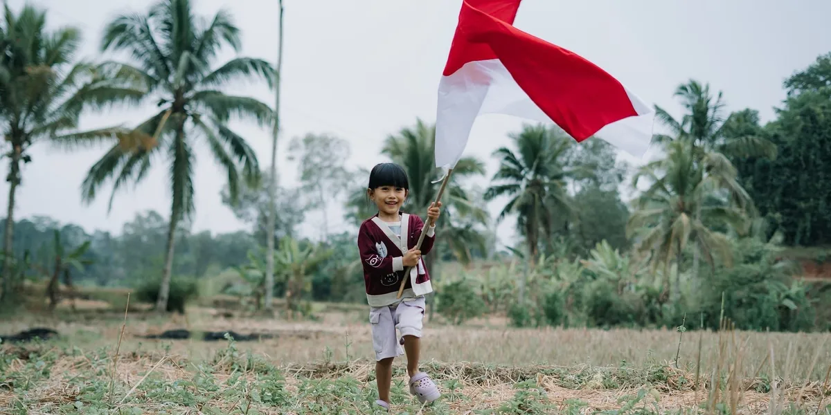 A young girl waving the Indonesian flag in a rice field lined with palm trees