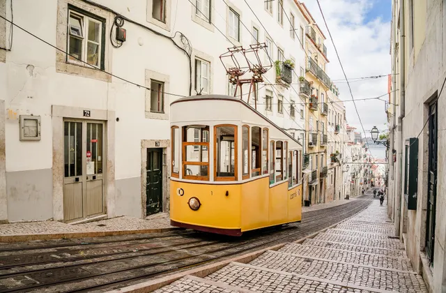 A yellow funicular tram climbing a narrow cobblestone street between whitewashed buildings in Lisbon