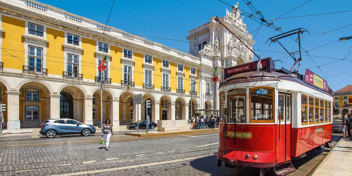 A vintage red tram passing the Praça do Comércio in Lisbon, Portugal