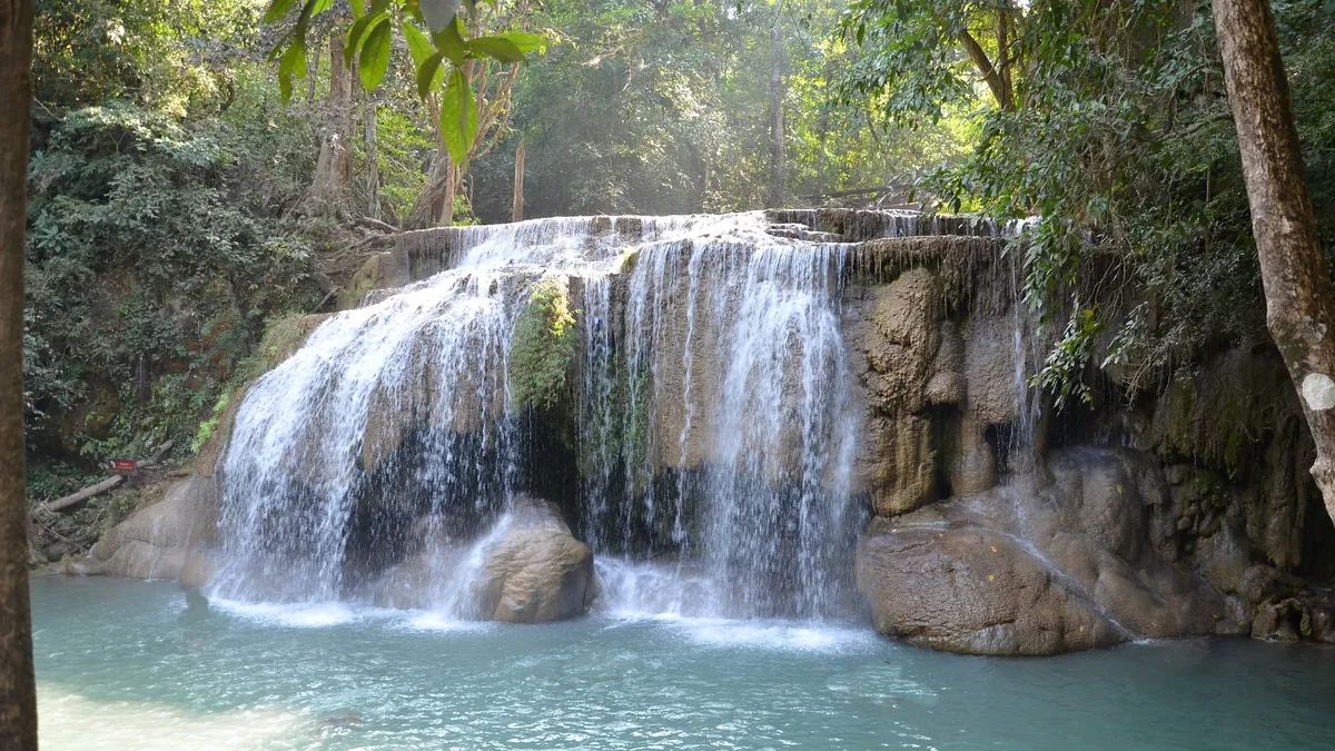 A waterfall cascading over tiered limestone rock into a turquoise pool surrounded by jungle