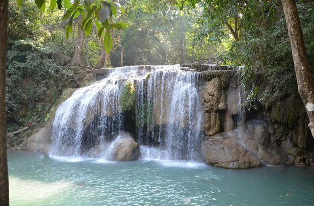 A waterfall cascading over tiered limestone rock into a turquoise pool surrounded by jungle